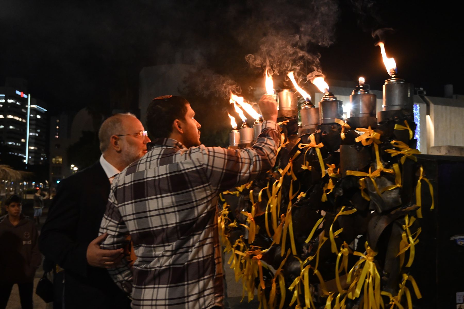 The Menorah of Hope lit at night in Hostages Square, its branches tied with yellow ribbons